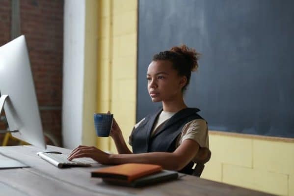 Een jonge vrouw werkt op een computer aan een bureau dat vlakbij het schoolbord staat in een leslokaal