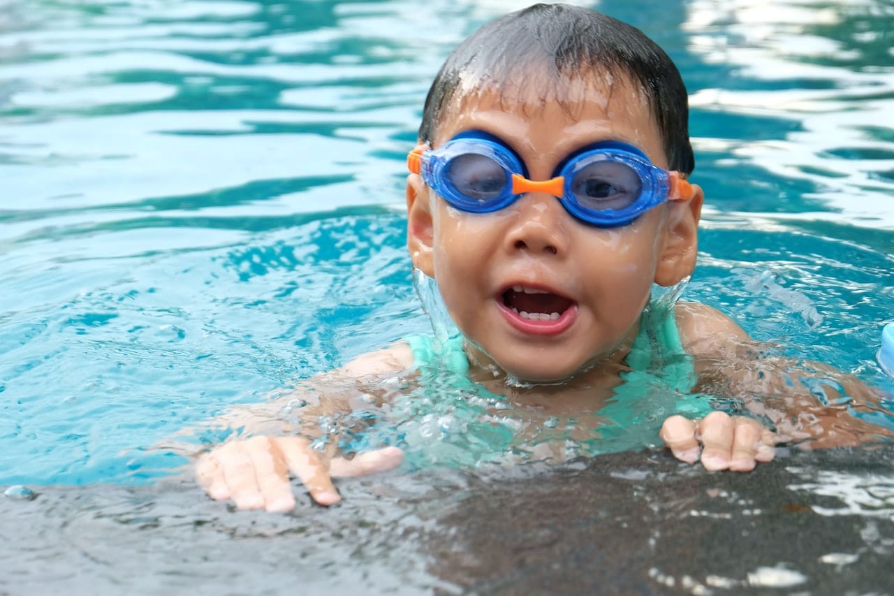 Een peuter met duikbril in het water, bij de zwembadrand