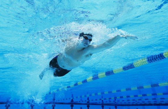Een zwemmer met duikbril en badmuts op trekt baantjes in een binnenzwembad